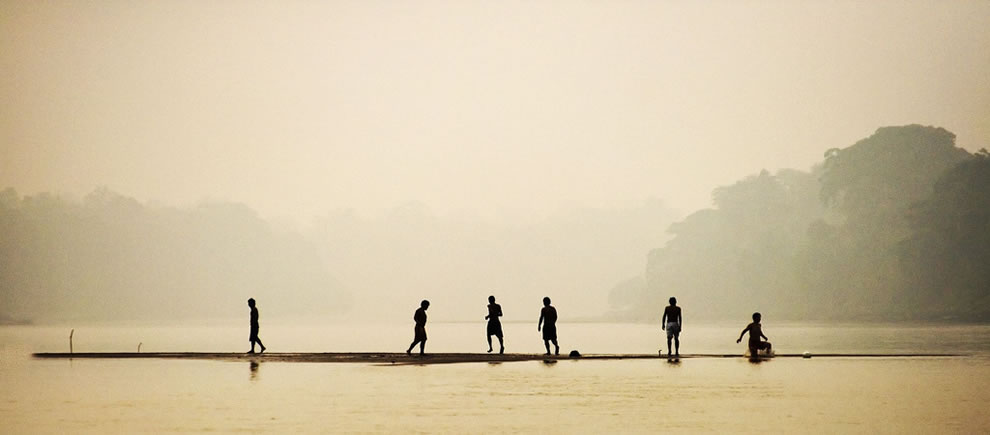 On the Tambopata River in the Peruivan Amazon Rainforest, a group of kids play football on a tiny sand island in the middle of the river